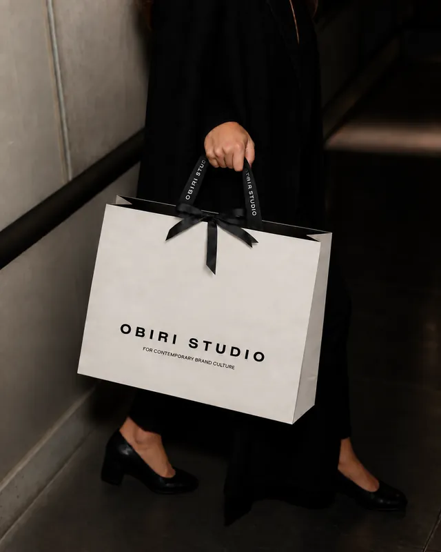 Elegáns OBIRI Studio ajándéktáska fekete szalaggal, átadás közben